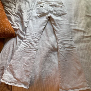 Vita Lois Raval high rise flare jeans - Säljer ett par vita Lois Raval jeans med hög midja och utsvängda ben. Klassisk femficksmodell med snygga detaljer och Lois-logga på fickan. Jeansen är tillverkade i Spanien och har en riktigt fräsch vibe, perfekta för dig som gillar retrostil och vill sticka ut.