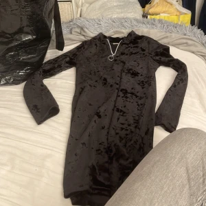 Svart sammetsklänning med lång ärm - Supersnygg svart sammetsklänning med lång ärm och enkel, rak passform. Klänningen har en mjuk, glansig yta som ger en lyxig känsla och funkar perfekt när du vill sticka ut lite extra. Klassisk och stilren look.