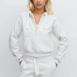 Ljusgrå hoodie med dragkedja - Säljer en ljusgrå hoodie med dragkedja och huva. Tröjan har snörning i huvan, två fickor framtill och ribbade muddar vid ärmslut och midja. Perfekt för en avslappnad och chill stil.