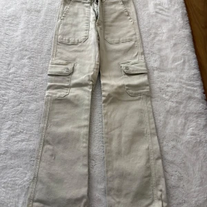 Beige cargopants med raka ben - Snygga beige cargopants med raka ben och stora fickor på sidorna. Byxorna har även fickor fram och bak samt knappar på ficklocken. Perfekta för en avslappnad och trendig stil.