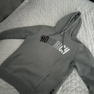Grå HOODRICH hoodie och byxor set - Säljer ett grått mjukisset från HOODRICH med matchande hoodie och byxor. Hoodien har stor magficka, dragsko i huvan och broderad logga i svart och silver på bröstet. Byxorna har resår och snörning i midjan samt HOODRICH-logga på låret.