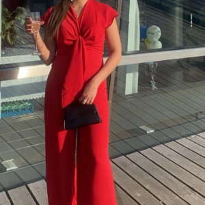 Röd långklänning med knyt framtill - Säljer en snygg röd långklänning från Mango med cool knytning framtill och v-ringad hals. Klänningen har korta ärmar och ett flowigt fall som ger en riktigt chic vibe. Använd endast en gång och säljer för att den inte passar mig längre. 