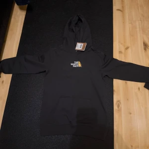 Svart hoodie från The North Face XL - Svart hoodie från The North Face i storlek XL Youth. Klassisk modell med huva, magficka och broderad logga på bröstet. Perfekt för chill dagar eller när du vill ha en enkel och stilren look.