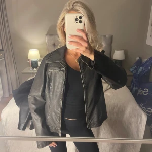 Svart/brun skinnjacka med dragkedja - Säljer en svart/brun/grå skinnjacka med klassisk krage och silverfärgad dragkedja framtill. Jackan har en ficka med dragkedja på bröstet och raka, lite loose ärmar. Aldrig använd