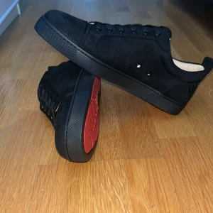 Svarta Christian Louboutin  - Snygga svarta sneakers från Christian Louboutin i mocka med klassisk röd sula och logga på hälen. Skorna var för små för mig därför så säljs de.
