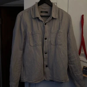 Beige overshirt Dressmann  - Stilren beige overshirt från Dressmann i storlek M. Skjortan har två bröstfickor, klassisk krage och knäppning framtill. Otroligt trevlig och bra passform samt att den passar till alla plagg. Nypris är 749, hör av er vid intresse!