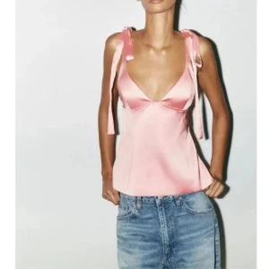 Zara Rosa satinlinnetopp med knytband - Supersöt rosa linnetopp i satin med v-ringning och breda axelband som knyts till rosetter på axlarna. Toppen har en lätt utsvängd passform och slät yta som ger en lyxig känsla. Perfekt för att lyfta vilken outfit som helst.