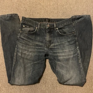 Mörkblå jeans från Hugo Boss - Säljer ett par jeans från Hugo Boss med snygg tvättad effekt och klassisk femficksdesign. Jeansen har raka ben och subtila slitningar framtill. Bra skick endast defekt höger ficka på baksidan se bild. Storlek 30/32. Är 184 lång och dem sitter bra. Bara att skriva vid frågor!😃
