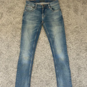 Blå skinny jeans från Nudie Jeans - Säljer ett par klassiska blå skinny jeans från Nudie Jeans i storlek W28 L32. Modellen är tight terry, jeansen har snygga slitningar och kontrastsömmar. Passformen är tight och materialet är stretchigt denim för extra komfort.