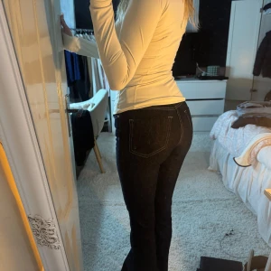 Mörkblå bootcut jeans med kontrastsömmar - Säljer ett par mörkblå jeans med bootcut-modell och snygga kontrastsömmar. Jeansen har låg midja och klassisk femficksdesign. Materialet är jeans med en tight passform upptill och lätt utsvängda ben. Perfekta för dig som gillar en tidlös och trendig look.