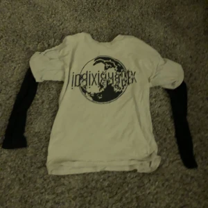 Vit och svart långärmad t-shirt med tryck - Vit t-shirt med svarta långa ärmar i lager-på-lager-stil. Framsidan har ett stort svart tryck med texten 'indixidualtex' och en grafisk jordglob. Skön passform och cool kontrast mellan ärmar och kropp. Perfekt för dig som gillar streetwear vibes.