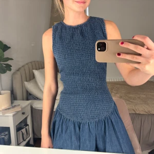 Blå jeansklänning  - Supersöt blå kort klänning från Zara i jeansmaterial med smockad överdel och ärmlös design. Klänningen är helt oanvänd .