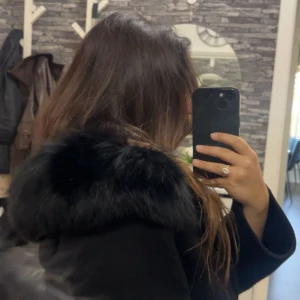 Svart kappa med fuskpäls - Säljer en svart kappa med päls krage. Jackan har bälte i midjan för snygg passform och stora fickor framtill. Pälsen runt händerna medföljer inte. Helt ny men säljer på grund av jag har liknande då jag fick denna som present. Priset kan diskuteras!