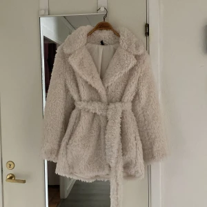Vit teddyjacka med bälte från H&M - Supermjuk och fluffig teddyjacka i vit från H&M. Jackan har bred krage, två knappar framtill och ett matchande bälte i midjan. Riktigt mysig för kyliga dagar, har fickor på vardera sida och tyvärr knapt blivit använd.