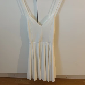 Studentklänning - Supersöt vit kort klänning från BikBok i storlek XS, passar även S. Används även som studentklänning! Klänningen har smala axelband, v-ringning och ett flowy kjolparti. Den sitter otroligt fint på midjan. Baksidan har snygga korsade band som ger en extra detalj. Perfekt för sommarens alla tillfällen eller studenten! Använd 1 gång.
