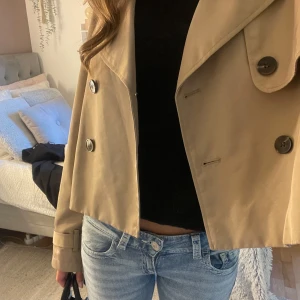 Beige croppad trenchcoat  - Säljer den här jättesnygga korta trenchcoat från H&M! Använd ett fåtal gånger så väldigt bra skick. Storlek M men passar mig perfekt som brukar ha XS/S, perfekt nu till hösten!💗🍂 