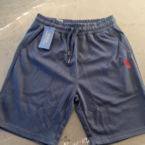 Blå shorts från Polo Ralph Lauren - Snygga marinblå shorts från Polo Ralph Lauren med röd broderad logga på benet. De har elastisk midja med snörning och är gjorda i mjuk bomull. Perfekta för chill dagar eller träning. Klassisk och enkel design med två sidofickor.