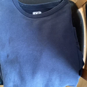 Mörkblå sweatshirt från CP - En stilren mörkblå sweatshirt från CP med rund halsringning och ribbade muddar. Perfekt för dig som gillar en enkel och klassisk look. Passar till det mesta och är superbekväm att bära.