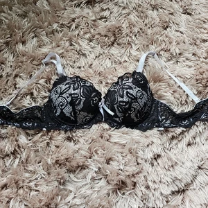 Svart spets-bh med vita detaljer 80B - Säljer en snygg svart bh med spets och vita detaljer. Kuporna är vadderade och har en cool struktur på insidan. Axelbanden är vita och justerbara och avtagbara. Bh:n är i storlek 80B.