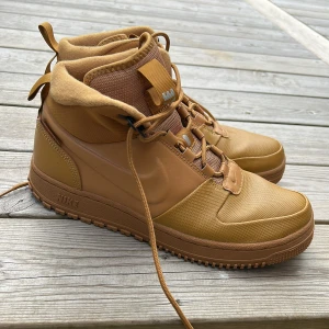 Nike bruna high-top sneakers - Snygga bruna high-top sneakers från Nike med robust sula och snörning. Skorna har en blandning av textil och syntetmaterial, perfekt för dig som gillar streetstyle och vill ha något som sticker ut. Klassisk Nike-logga på sidan och detaljer på plösen.