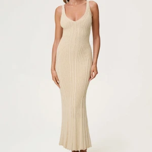 Beige ribbad lång stickad klänning från Adoore  - Supersnygg beige långklänning i ribbstickat material med v-ringning och breda axelband. Klänningen har en figurnära passform som framhäver siluetten och en lätt utsvängd nederdel. Perfekt för dig som gillar en stilren och trendig look.