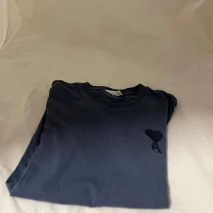 Blå t-shirt från Ami Paris med hjärtdetalj - Snygg marinblå t-shirt från Ami Paris med broderad hjärtdetalj och bokstaven A på bröstet. Klassisk rund halsringning och korta ärmar. Tillverkad i mjuk bomull för en skön känsla hela dagen.