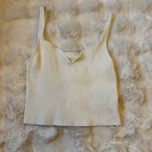 Ribbad vit linnetopp från H&M - Superfin ribbad linnetopp från H&M i vitt. Toppen har breda axelband, en liten v-ringning framtill och är croppad i modellen. Perfekt att styla med jeans eller kjol för en fräsch look. Materialet är mjukt och stretchigt för extra komfort.