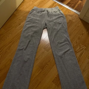 Grå mjukisbyxor med fickor och snörning - Mysiga grå mjukisbyxor från Juicy Couture med raka ben, snörning i midjan och stora fickor både fram och bak. Bakfickorna har snygga knappar och på ena framfickan finns en broderad JC-logga. Perfekta för chill dagar eller när du vill vara bekväm. Priset går att  diskutera 
