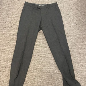 Kostymbyxor | OSCAR JACOBSON. - Snygga grå kostymbyxor från Oscar Jacobson i klassisk rak modell. Byxorna är tillverkade i ett mjukt och stilrent tyg som passar perfekt till en dressad look. Perfekta för dig som gillar stilrena och tidlösa plagg.