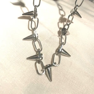 Coolt nithalsband-Montini- #punk #rock #alternative - Säljer ett snyggt och rejält halsband i nyskick,med nitar från märket Montini. . Det funkar lika bra som ett statement-plagg till vardags som till festivaler eller konserter. Halsbandet är tillverkat i silverfärgad metall och har en bra tyngd som känns solid. Det är i mycket gott skick, precis som du ser på foton. Perfekt som present eller julklapp till någon som gillar att synas och göra sin klädsel.Mått Längd: 52 cm (inklusive förlängningskedjan) • Nithöjd: 2 cm • Vikt: 76 gram