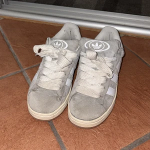 Adidas Campus grå sneakers! - Säljer ett par Adidas Campus sneakers i ljusgrå mocka med vita ränder och logga på tungan och hälen. Dom är använda några få gånger. Men det är absolut inget fel på dom! Priset kan diskuteras☺️💓