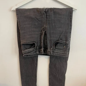 Svarta jeans från BLK DNM - Snygga gråa jeans från BLK DNM med klassisk femficksdesign och dragkedja. Jeansen har en mörk tvätt och raka ben, perfekta för en stilren look. Finns en del hål som går att laga annars kan man använda tyget för att tillverka annat roligt.
