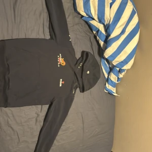 Svart hoodie sail Racing - Svart hoodie från Bahco Racing med broderade loggor på bröstet och ärmarna. Stor ficka framtill och huva med tryckt detalj. Perfekt för dig som gillar motorsport och vill ha en snygg och bekväm tröja med coola detaljer.