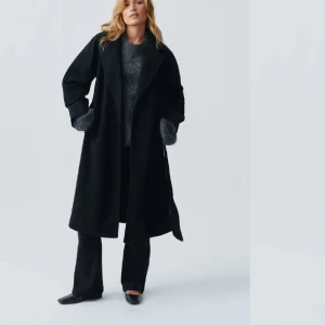 Svart lång kappa med bälte ginatricot - Snygg svart kappa med klassisk krage och bälte i midjan. Modellen är lång och har raka ärmar, vilket ger en chill och stilren vibe. Perfekt för dig som gillar minimalistisk look och vill ha en jacka som funkar till många outfits. Gina kappa pris kan alltid diskuteras 