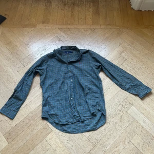 Rutig skjorta från Ralph Lauren - Snygg rutig skjorta från Ralph Lauren i blå och gröna toner med klassisk krage och knäppning framtill. Skjortan har lång ärm och ikonisk rosa logga broderad på bröstet. Tillverkad i mjuk bomull som känns skön mot huden.