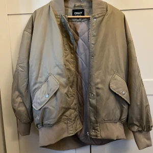Beige bomberjacka från ONLY - Säljer en beige bomberjacka från ONLY med quiltat foder, två stora fickor med lock och tryckknappar samt ribbade muddar vid ärmslut och midja. Jackan har dragkedja framtill och en oversized passform, as snygg enligt mig!! 