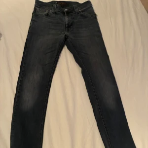 Mörkblå jeans från Nudie Jeans Co - Säljer ett par mörkblå jeans från Nudie Jeans Co i storlek 29/32. Jeansen har klassisk femficksdesign, raka ben och subtila slitningar för en snygg look. Tillverkade i mjukt denimtyg som sitter skönt hela dagen.
