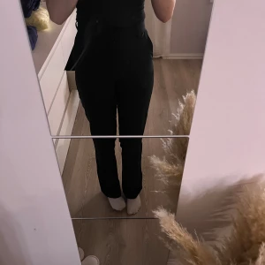 Svarta kostymbyxor med rak passform - Säljer ett par svarta kostymbyxor med hög midja och rak passform. Byxorna har klassisk design med fickor i sidorna och stängs med knapp och dragkedja. Perfekta för en clean och stilren look.