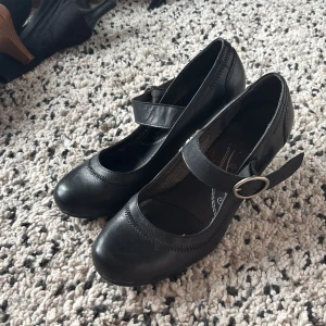 Svarta Mary Jane pumps med klack - Säljer ett par svarta Mary Jane pumps från Flexi i skinn med rund tå och snygg rem med silverfärgat spänne. Skorna har låg klack och klassisk design som passar till många olika outfits. Perfekta för dig som gillar stilrena och bekväma skor. Sköna att gå i och passar för många tillfällen! Skriv för frågor pris går att diskutera!!💗