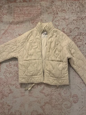 Beige quiltad teddyjacka från Zara - Quiltad teddyjacka från Zara i beige med hög krage och stora fickor framtill. 
