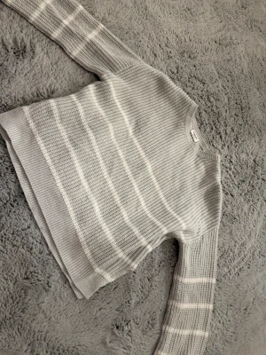 Grå vit randig stickad tröja  - En grå vit randig stickad tröja från Kappahl i storlek 146. Upplevs stor i storleken. Snitt där nere på sidorna. 