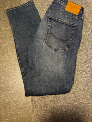 Blå slim straight jeans från Jack and Jones  - Säljer ett par klassiska blå jeans från Nudie i modellen Slim Straight/Tim. Jeansen har en rak passform med smal siluett, fem fickor och snygga kontrastsömmar. Tillverkade i slitstark bomull med en tidlös tvätt.