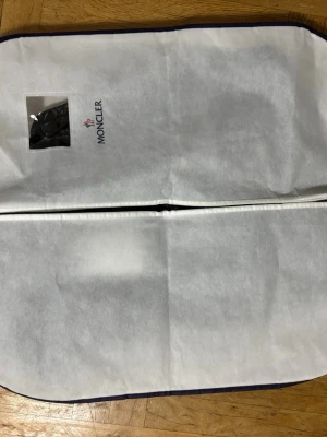 Svart dunväst från Moncler med huva - Snygg svart dunväst från Moncler med glansig finish och huva. Västen har dragkedja framtill, två fickor med dragkedja och Moncler-logga på bröstet. Perfekt för lager-på-lager och streetstyle. Levereras med original fodral och taggar.