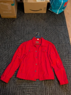 Röd jeansjacka – som ny – passar M/L - Säljer en röd jeansjacka i mycket fint skick. Använd max 1 gång, i princip som ny. Snygg distressed/sliten design som ger en cool streetwear-look. 🔸 Märkt 4XL, men passar snarare M/L 🔸 Färg: röd 🔸 Knäppning framtill + bröstfickor 🔸 Inget slitage förutom designen 🔸 Rök- och djurfritt hem Pris: 150 kr Kan skickas mot frakt eller hämtas upp enligt överenskommelse. Hör av dig vid intresse!