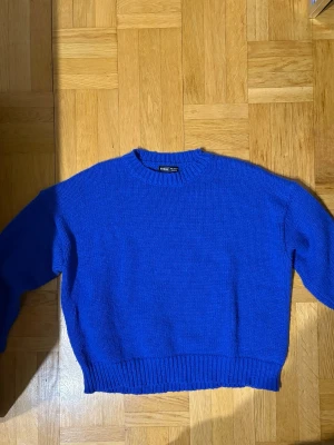 Kornblå stickad tröja från Shein - En kornblå stickad tröja från Shein med avslappnad passform och rund halsringning. Tröjan har ribbstickade muddar vid ärmslut och nederkant, vilket ger en snygg och enkel look. Perfekt att styla med jeans för en cool vardagsstil.