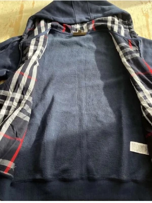 Marinblå hoodie från Burberry - Snygg marinblå hoodie med dragkedja från Burberry. Insidan av huvan har det klassiska rutmönstret i svart, vitt och rött. Priset kan diskuteras 