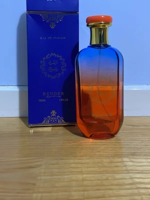 Render Eau de Parfum 100ml - Parfymflaska från Render med en snygg blå och orange glasdesign och gulddetaljer. Flaskan rymmer 100 ml och har en elegant, modern look med orange kork. Kommer i en lyxig blå förpackning med gulddetaljer och text.