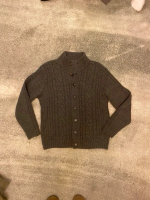 Mörkgrå stickad kofta Mauro Ferrini - Riktigt Snygg mörkgrå stickad kofta från Mauro Ferrini med kabelstickat mönster, ribbad krage och knäppning framtill. Vid funderingar, fråga på! 