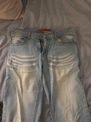 Ljusblå jeans från ONLY med raka ben - Säljer ett par ljusblå jeans från ONLY med raka ben och klassisk femficksmodell. Jeansen har slitningar och ljusa tvättade partier framtill för en trendig look. Tillverkade i jeansmaterial med knappgylf och bälteshällor.