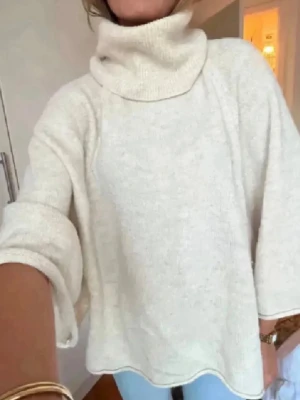 Beige polotröja med vida ärmar - Mysig beige stickad polotröja, insydd vid slutet för en snyggare passform. Tröjan har bred polokrage, långa ärmar och är tillverkad i ett mjukt, fluffigt material. Perfekt för lager på lager och en chill look. 